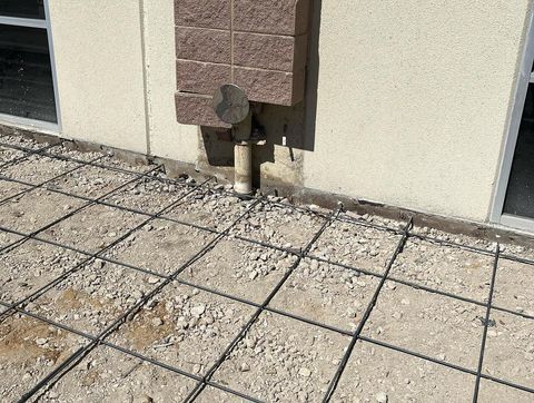 Building wall with a utility pipe and cracked concrete walkway below.