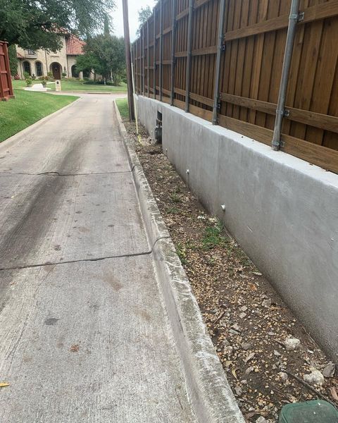 Concrete street beside a wooden fence and house, with a narrow dirt strip along the curb.
