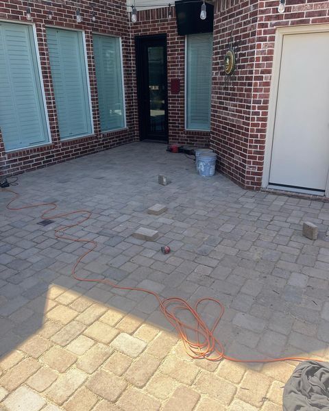 Brick courtyard with gray pavers, white shutters, a black doorway, and a bucket near the wall.
