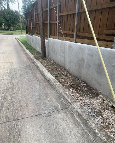 Concrete roadside beside wooden fence with a yellow support pole and narrow gravel strip.
