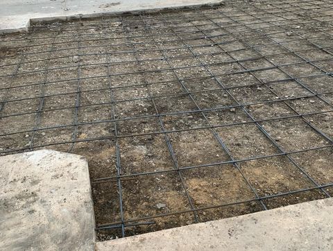 Concrete slab with steel rebar grid laid over compacted ground, ready for pouring.