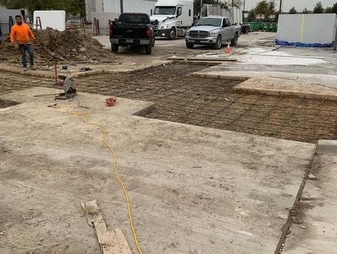 Construction site with muddy concrete, parked trucks, and a worker in an orange shirt