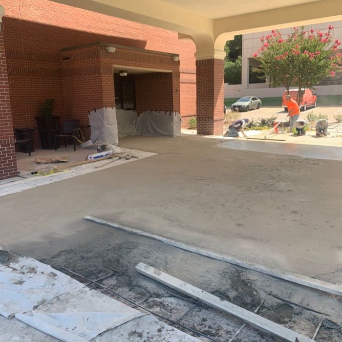 Construction workers resurfacing a driveway under a brick building’s covered entrance