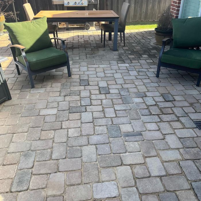 Patio with stone pavers, green cushioned chairs, and a wooden table in a backyard.