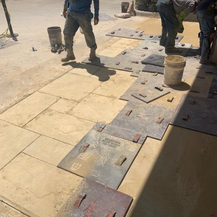 Workers installing large square floor tiles on a dusty construction site