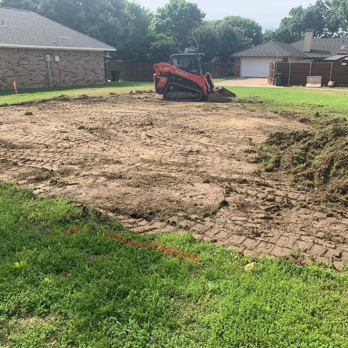 Red skid steer clearing a muddy backyard lot beside suburban houses