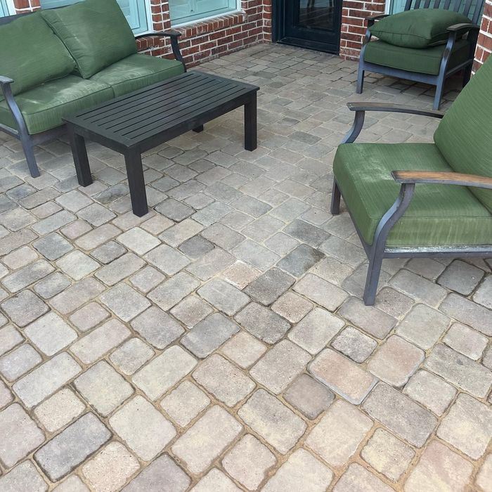 Patio seating area with green-cushioned chairs and a dark coffee table on a stone paver floor