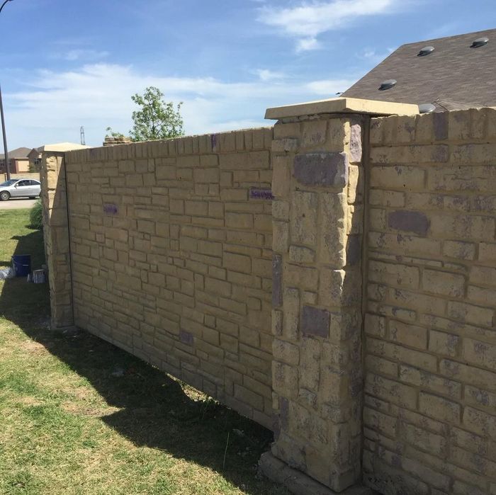 Stone and brick backyard wall with a pillar beside a grassy yard under a blue sky