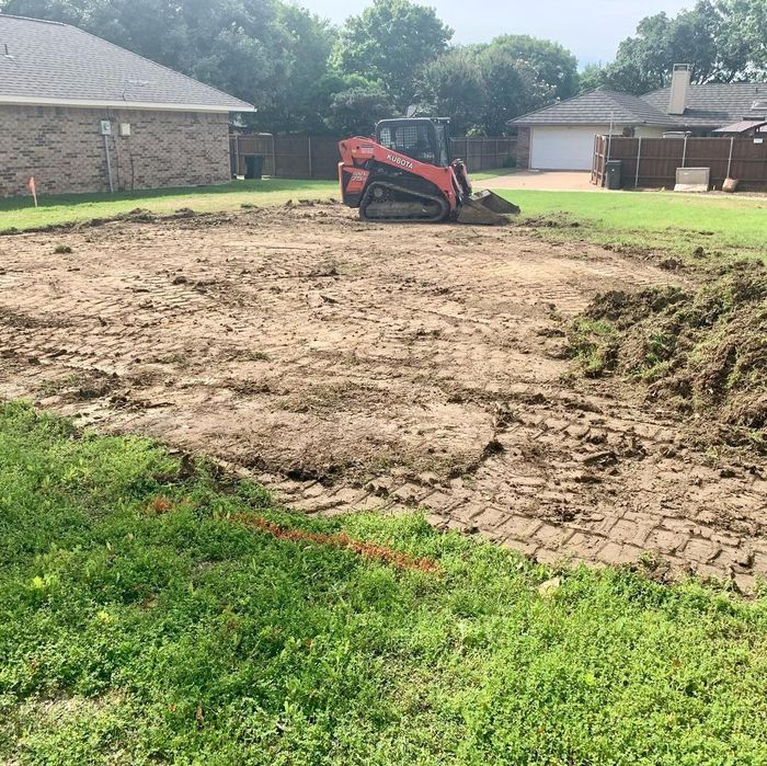 Excavator on a dirt-cleared lot in a suburban backyard, with grass and houses nearby.