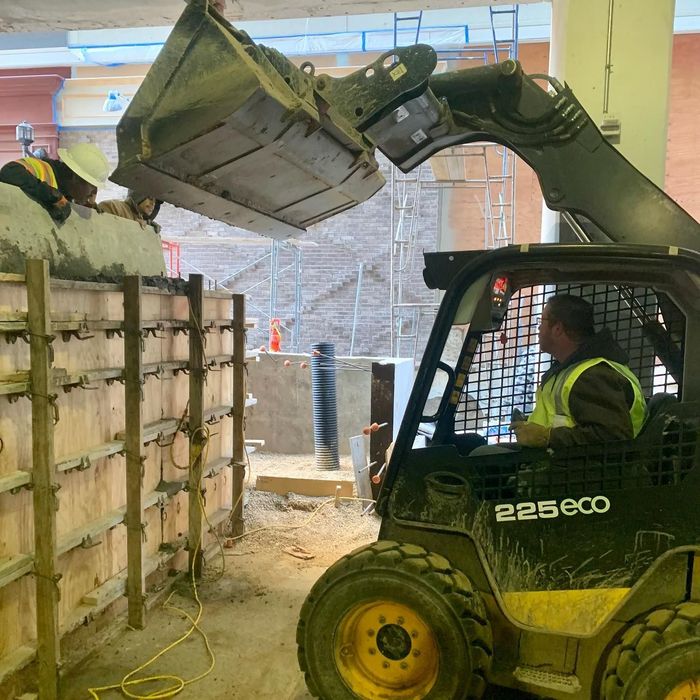 Compact loader lifting debris at a construction site, with a worker in a high-visibility vest inside the cab.