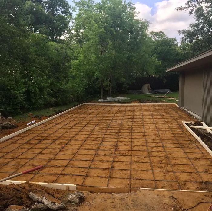 Concrete patio foundation under construction in a backyard, with rebar grid and surrounding trees