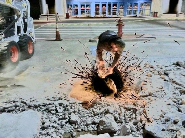 Construction worker breaking concrete with a jackhammer, sending debris flying on a street