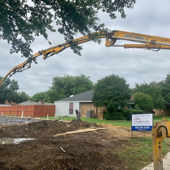 Concrete pump truck pouring at a residential construction site beside a small white house.