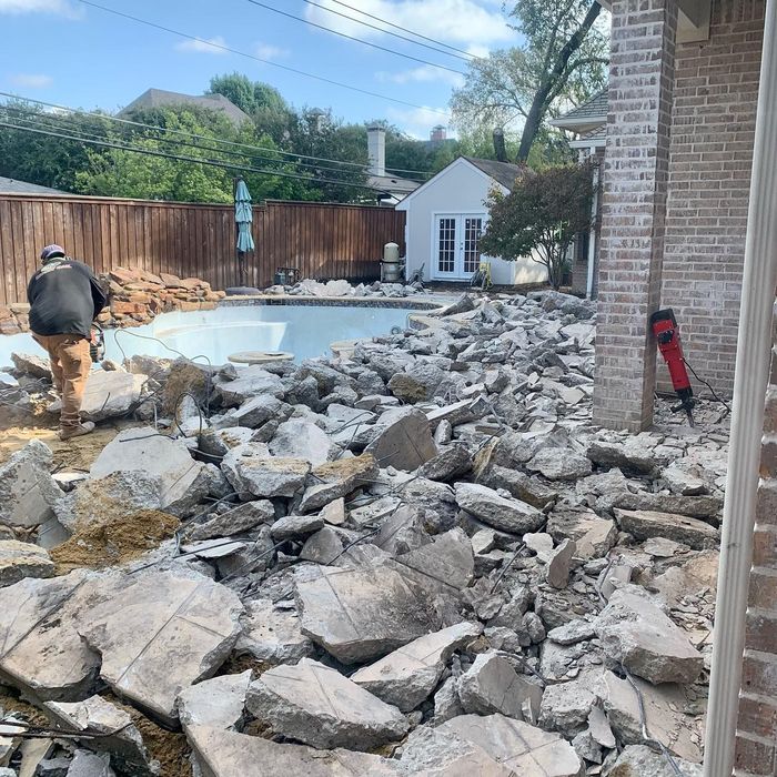 Backyard pool renovation with broken concrete rubble piled around the pool and a worker nearby