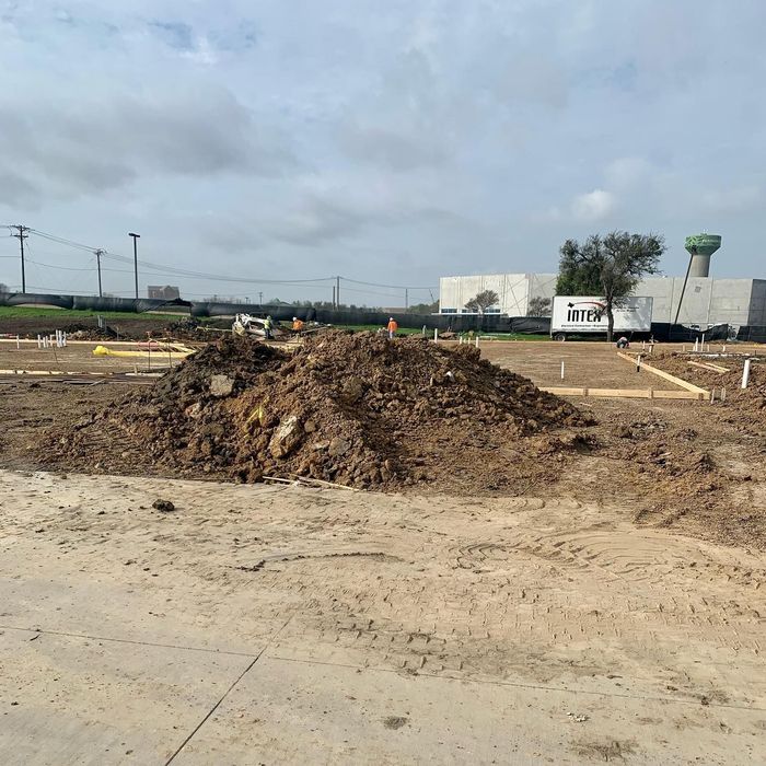 Construction site with dirt piles, marked ground, and a cloudy sky in the background