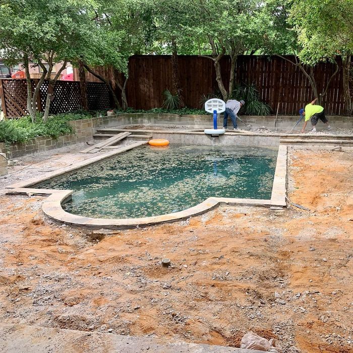 Backyard pool under construction, with two workers and muddy ground around the unfinished pool.