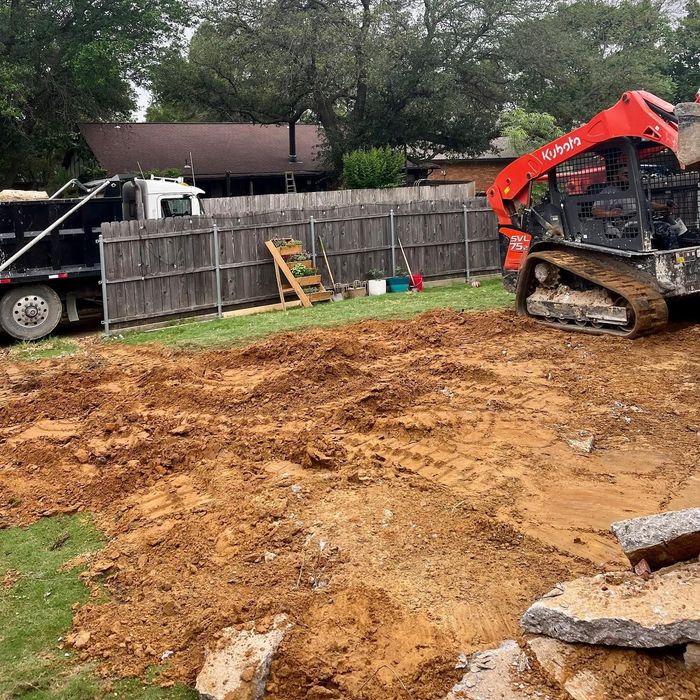 Backyard construction site with excavator, dump truck, and a wooden fence along the edge
