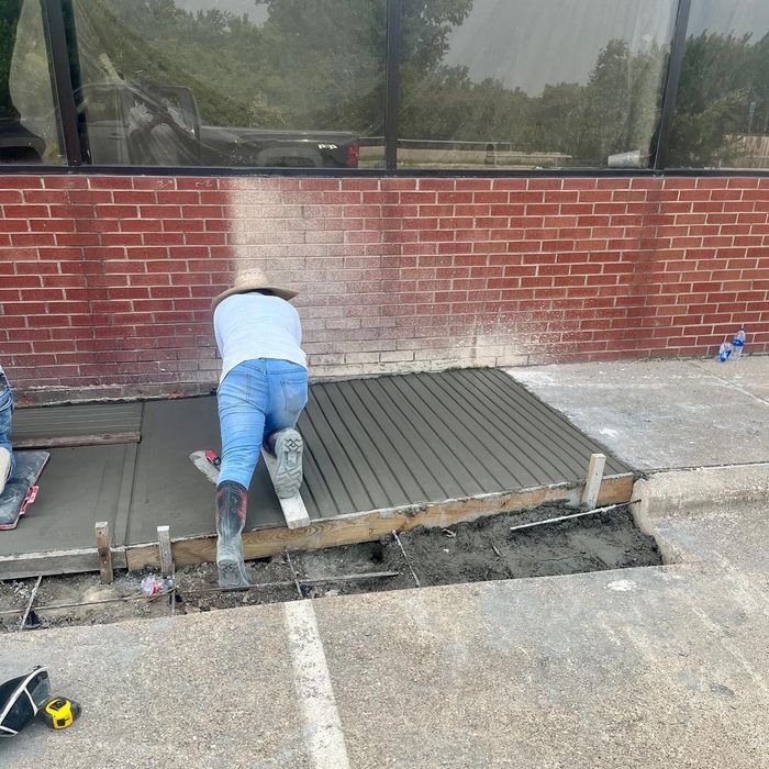 Worker kneeling while installing a gray ramp or walkway beside a brick building under construction