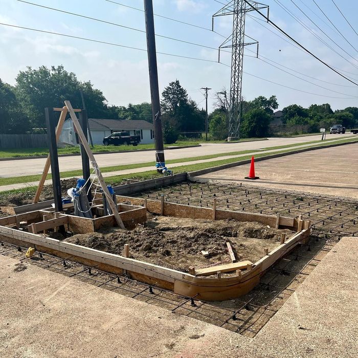 Roadside utility trench excavation with wooden forms, cones, and power lines under a clear sky