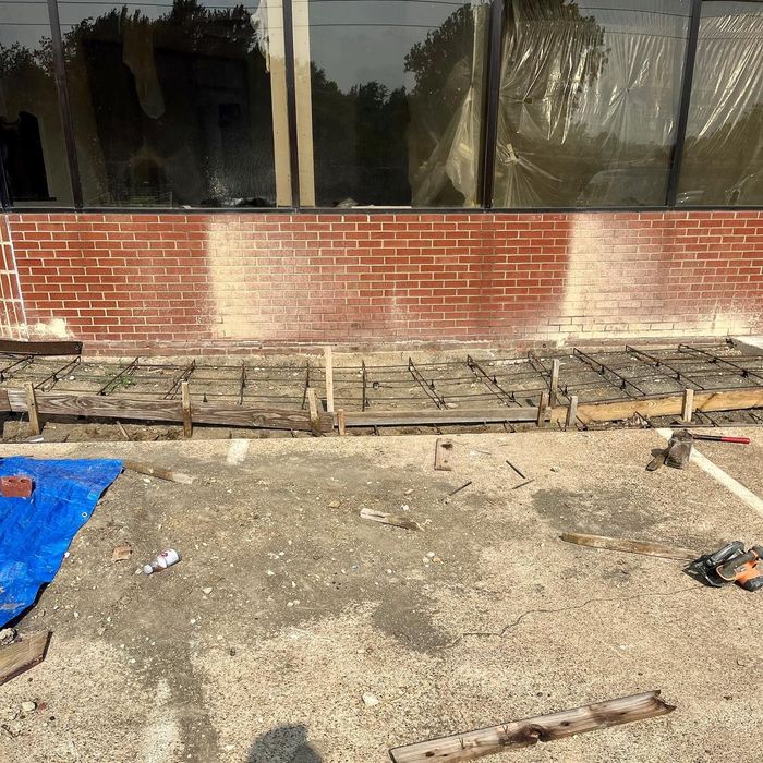 Construction site beside brick building with window reflections and wooden formwork on the ground.