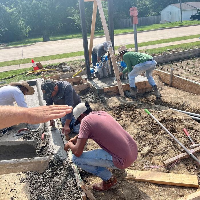 Workers pour and level concrete at a sidewalk construction site, with tools and boards around them.