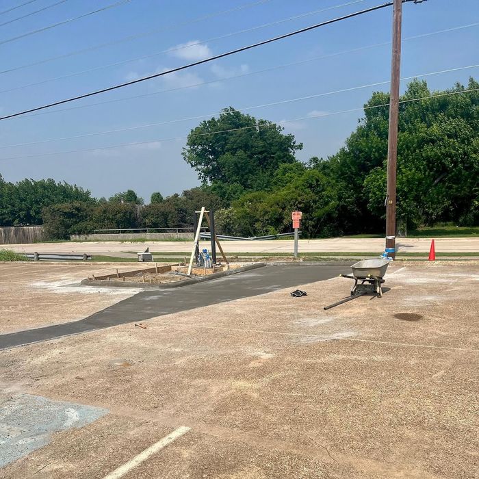 Parking lot with a portable sink, wheelbarrow, cones, and a small stream of water on the pavement.