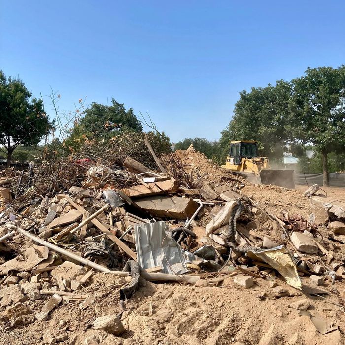 Bulldozer pushing debris at a demolition site with piles of rubble under a clear blue sky