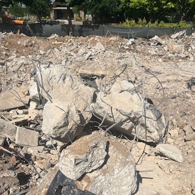 Pile of broken concrete rubble and exposed rebar at a demolition site under trees