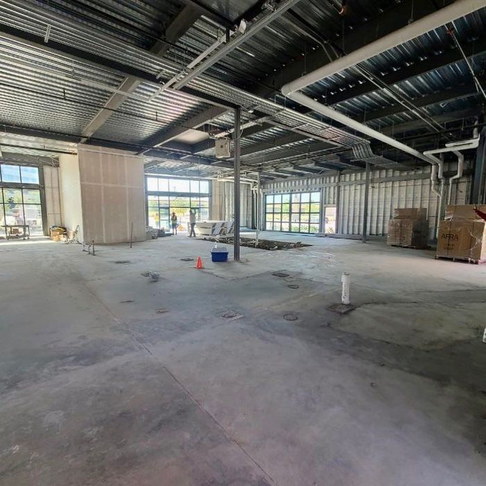 Empty industrial warehouse interior with exposed ceiling beams, concrete floor, and stacked materials near windows