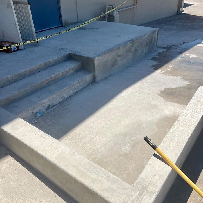 Concrete loading dock with steps and yellow caution tape, partially cordoned off in bright sunlight.