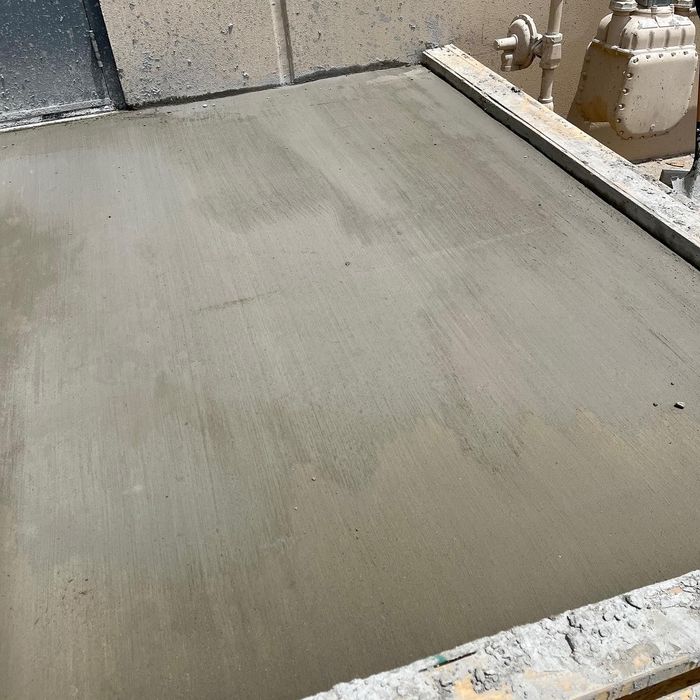 Freshly poured gray concrete slab at a construction site with rough edges and equipment nearby