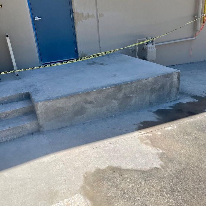 Concrete ramp and steps leading to a blue door, with caution tape across the entrance.