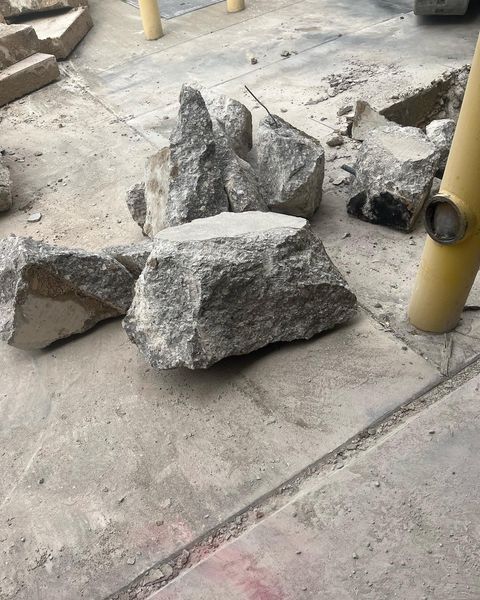 Broken concrete slabs scattered on a sidewalk beside yellow poles.