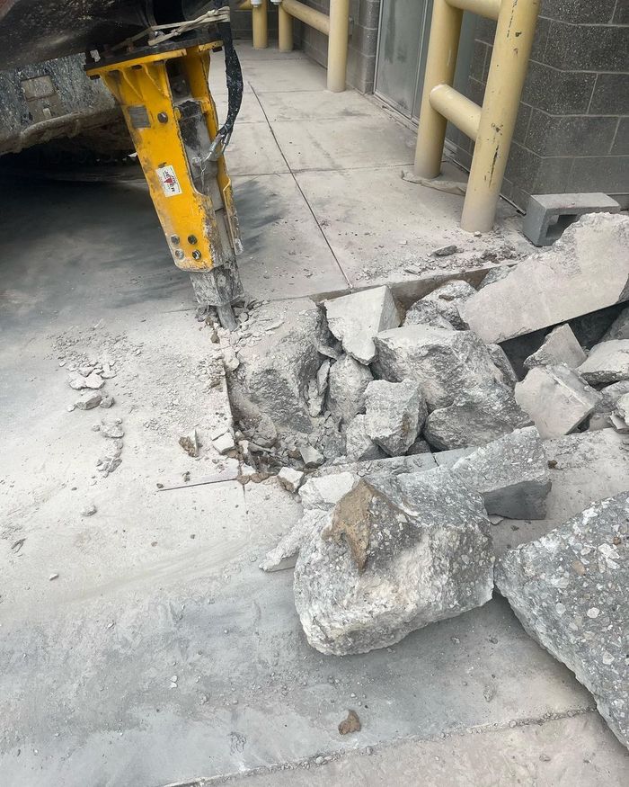 Yellow jackhammer breaking concrete beside a pile of rubble on a dusty floor