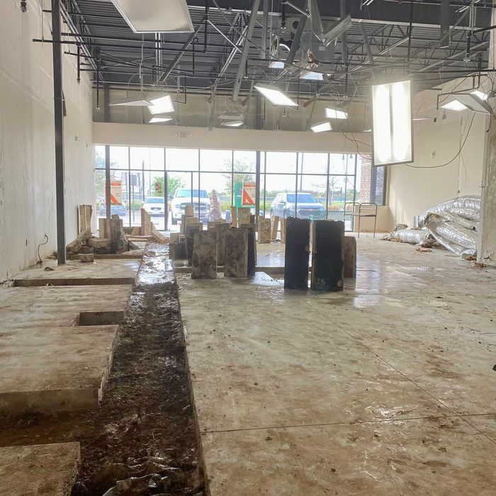 Empty retail space under renovation with exposed ceiling, concrete floor, and construction materials.