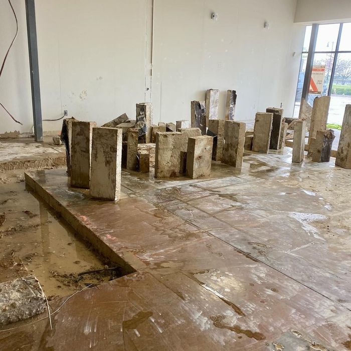 Indoor room with a wet concrete floor and scattered upright concrete blocks and columns.