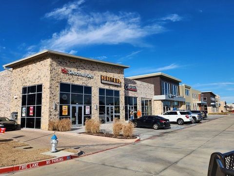Modern strip mall with stone storefronts, parked cars, and a bright blue sky