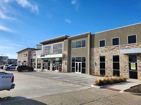 Modern two-story commercial building with stone facade, glass storefronts, and parked vehicles under a blue sky