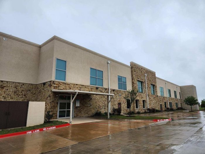 Stone building exterior with blue windows and a covered entrance on a rainy day