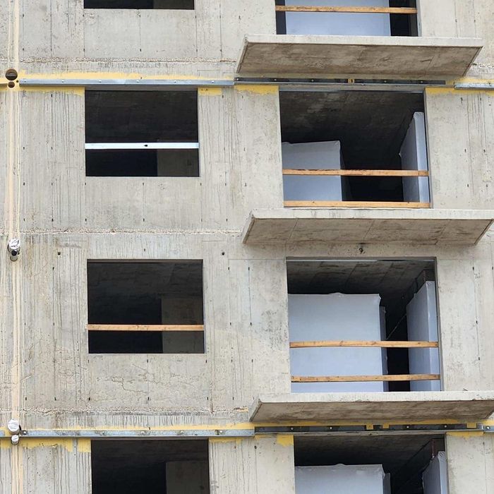 Concrete building facade with unfinished windows, balconies, and exposed construction supports