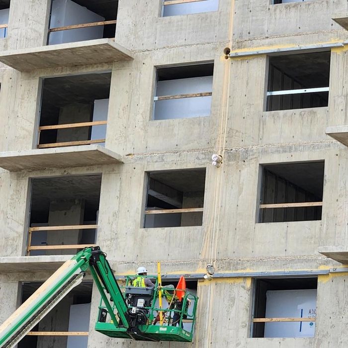 Construction workers on a green lift beside a concrete building under construction.