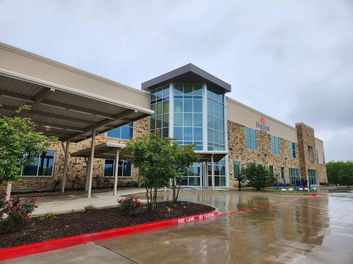 Modern office building entrance with glass atrium, covered parking, and wet pavement after rain