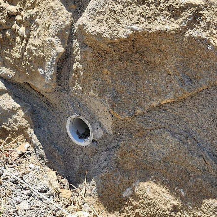 Close-up of a rock face with a small white circular pipe or hole embedded in it.
