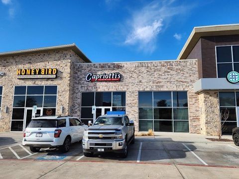 Strip mall storefronts for Honeybird and Capriotti’s with two parked pickup trucks under a blue sky