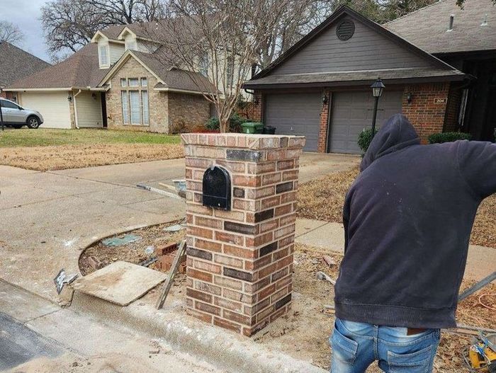 Brick mailbox on a suburban street, with a person in a dark hoodie standing nearby.