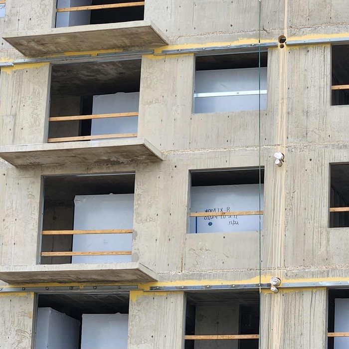 Concrete building facade with open window bays and temporary wooden railings under construction