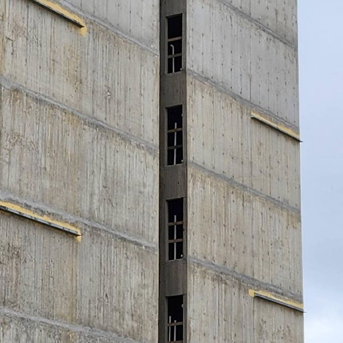 Concrete building facade with vertical strip of narrow windows and yellow trim lines