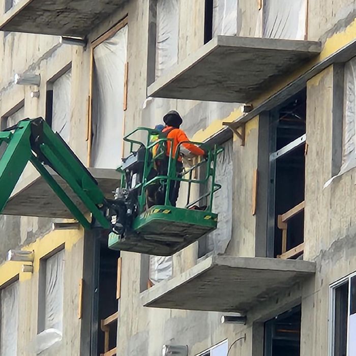 Worker in orange vest on green lift repairing a building facade with balconies and windows