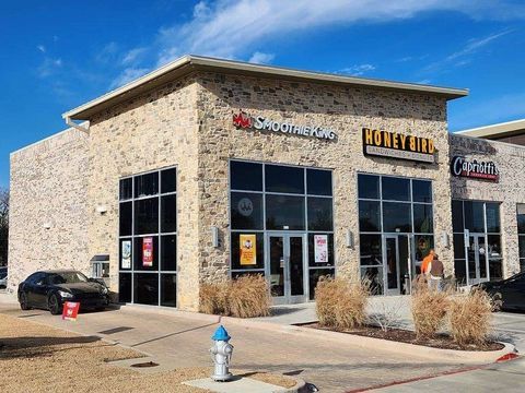 Stone storefront with large windows and signage, parked car outside on a sunny day.