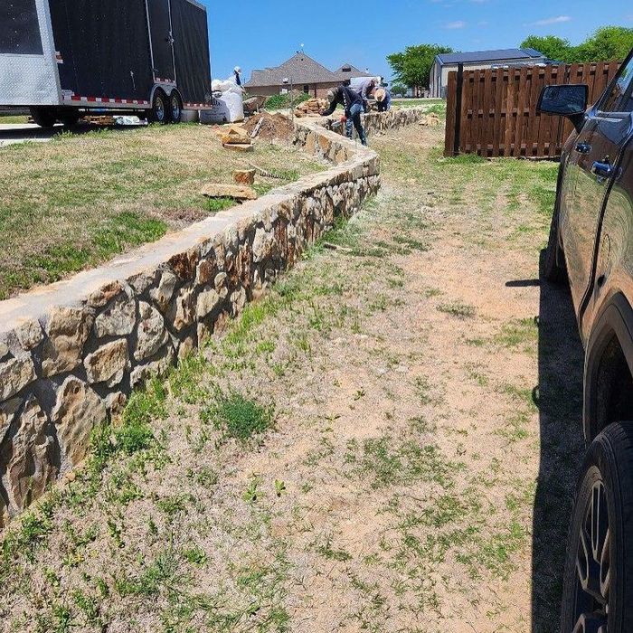 Stone retaining wall along a dirt path beside parked vehicles at a sunny construction site